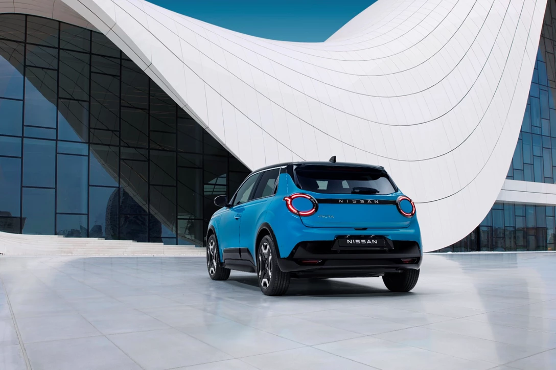 1709113-hero shot - rear 7_8 view of new Micra in blue gear color in front of a white & blue design architectural building.jpg